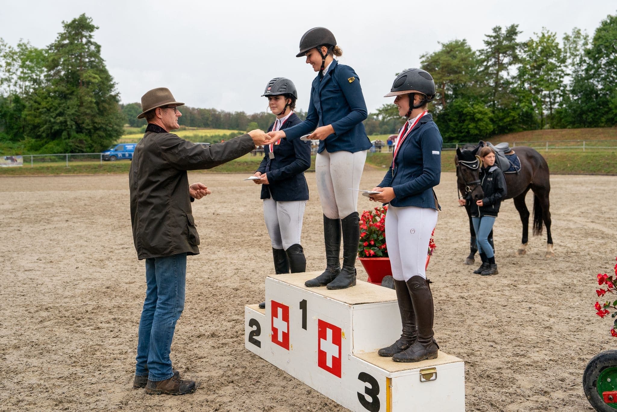Drei Reiterinnen auf einem Schweizer Springturnier-Podest mit Schweizer Kreuz, sportliche Anerkennung in der Schweizer Reitwelt